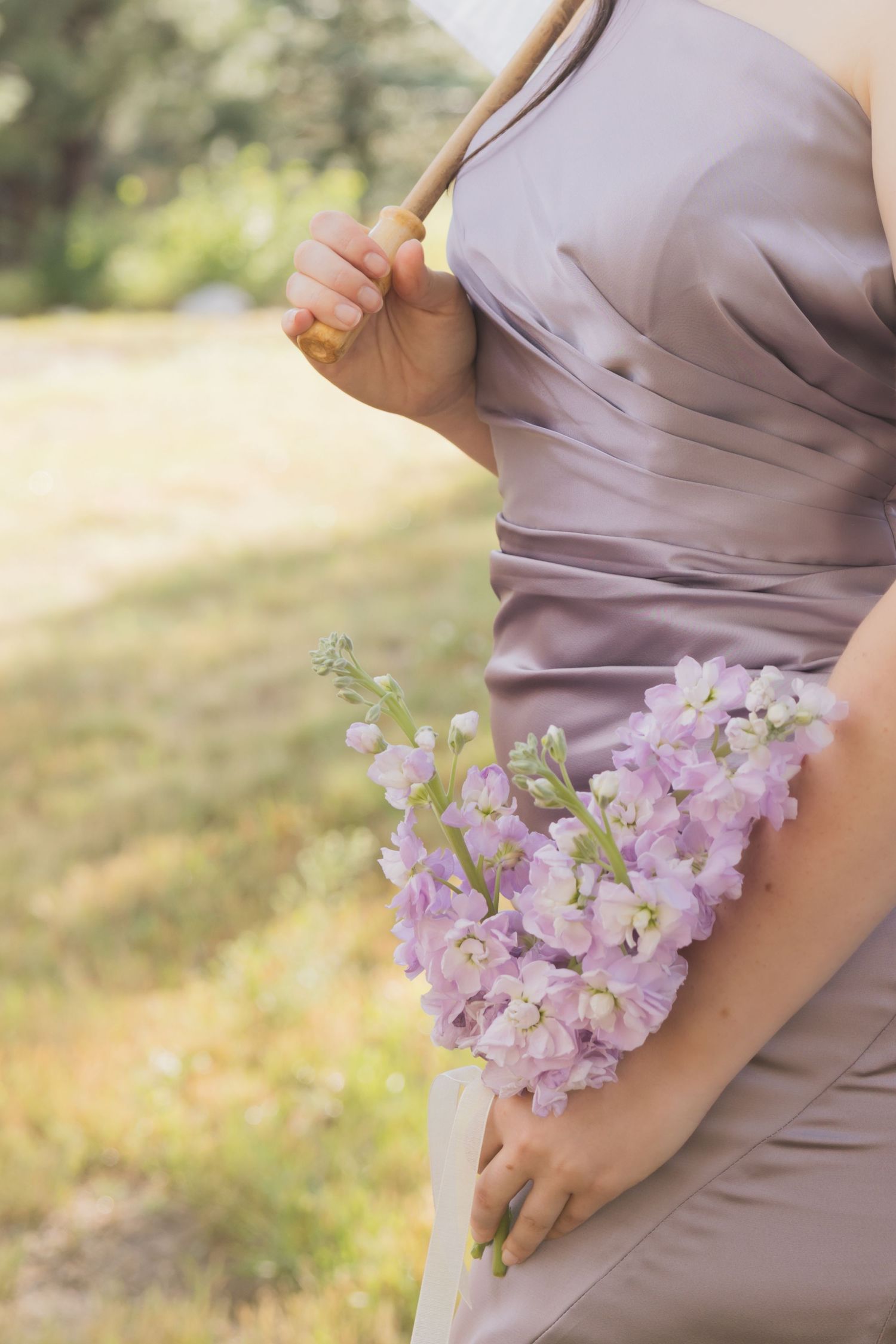 Delicate purple flowers held against a soft mauve dress in natural outdoor lighting.