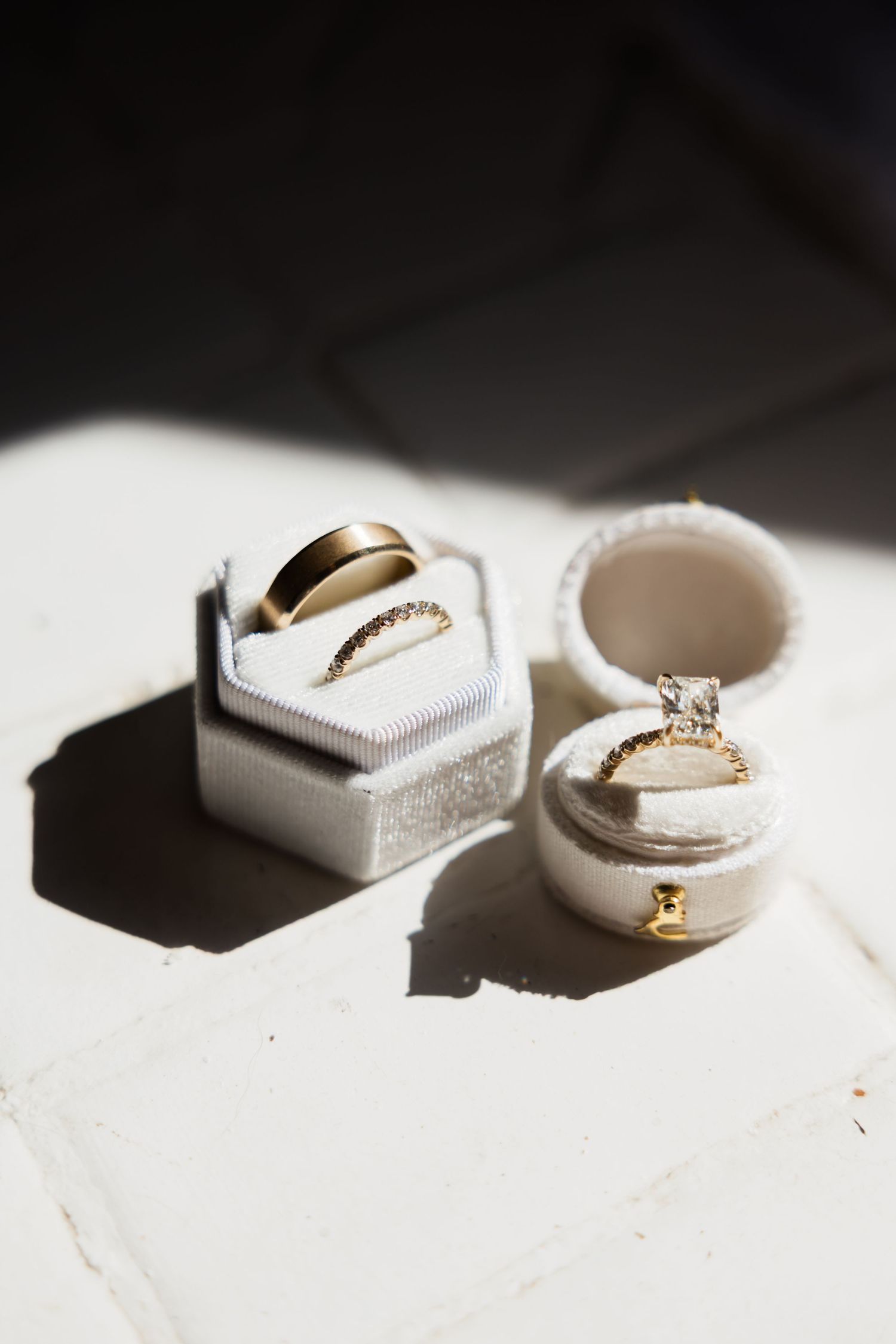 Wedding rings and jewelry displayed on white surface with dramatic shadows.