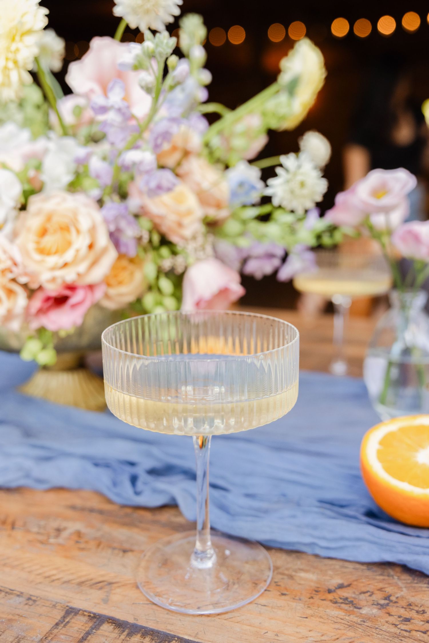 Elegant coupe champagne glasses on a blue table runner with floral decorations.