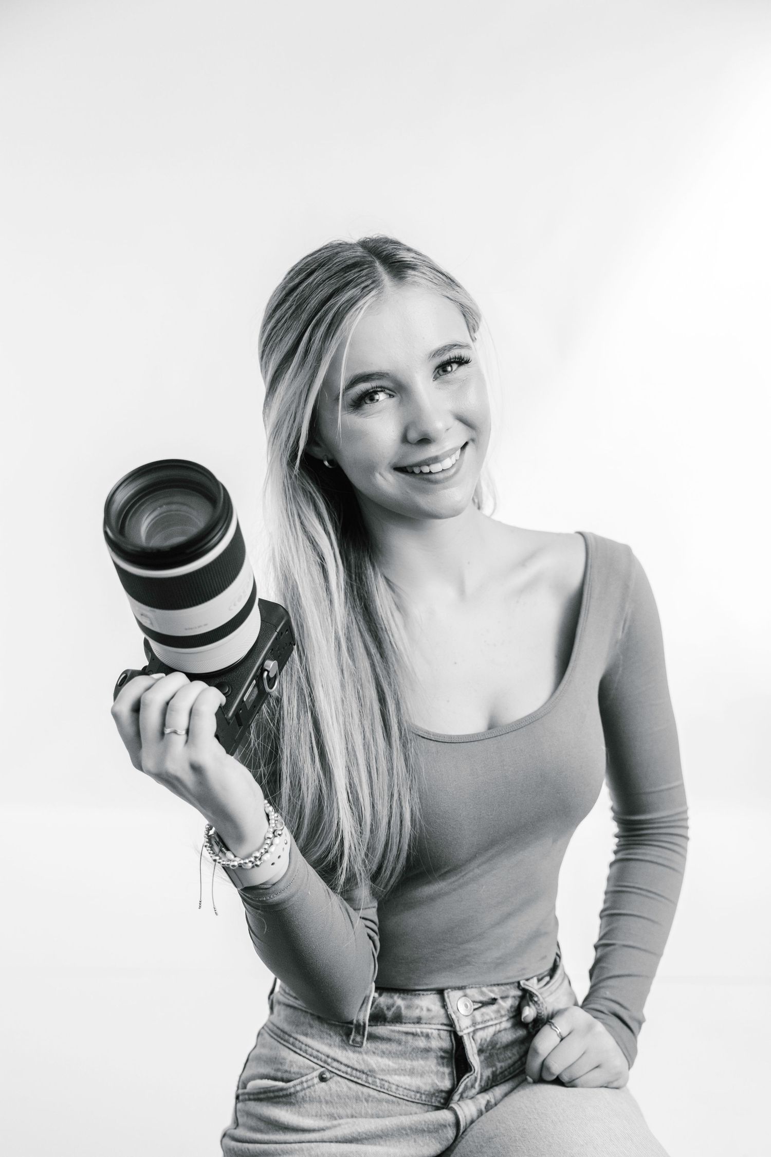 Person in casual attire holding a camera lens in a bright studio setting.