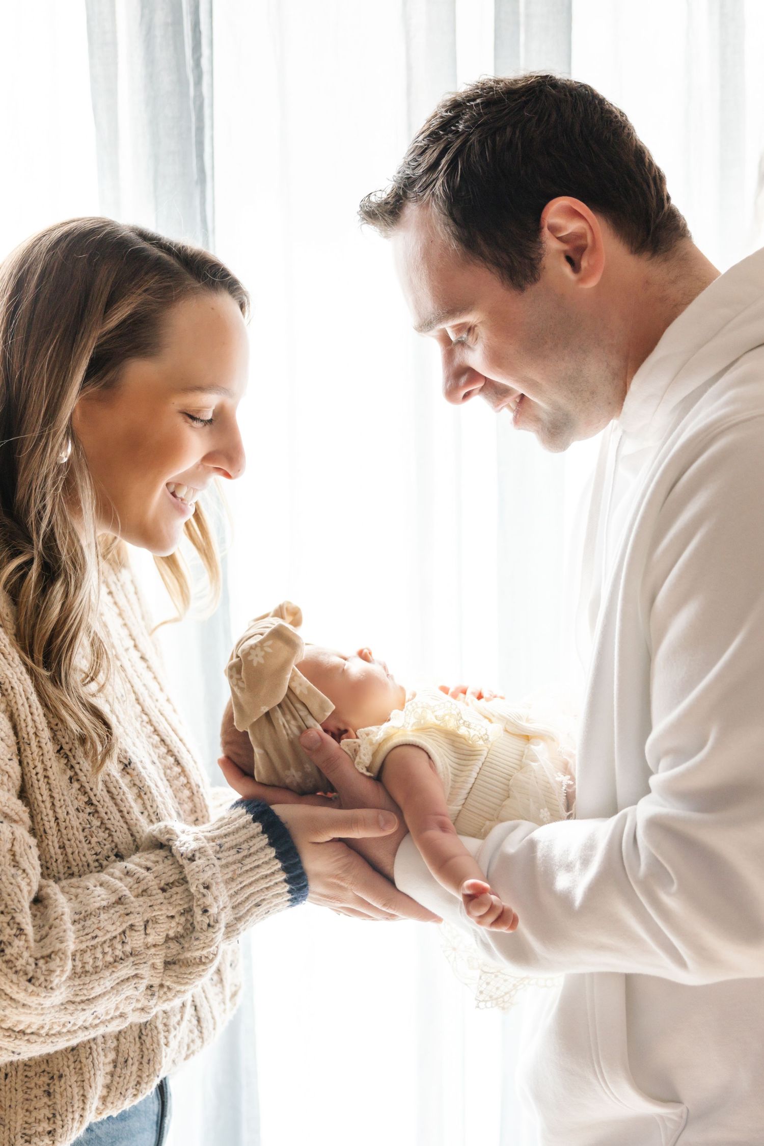 New parents sharing tender moment with newborn baby by bright window.