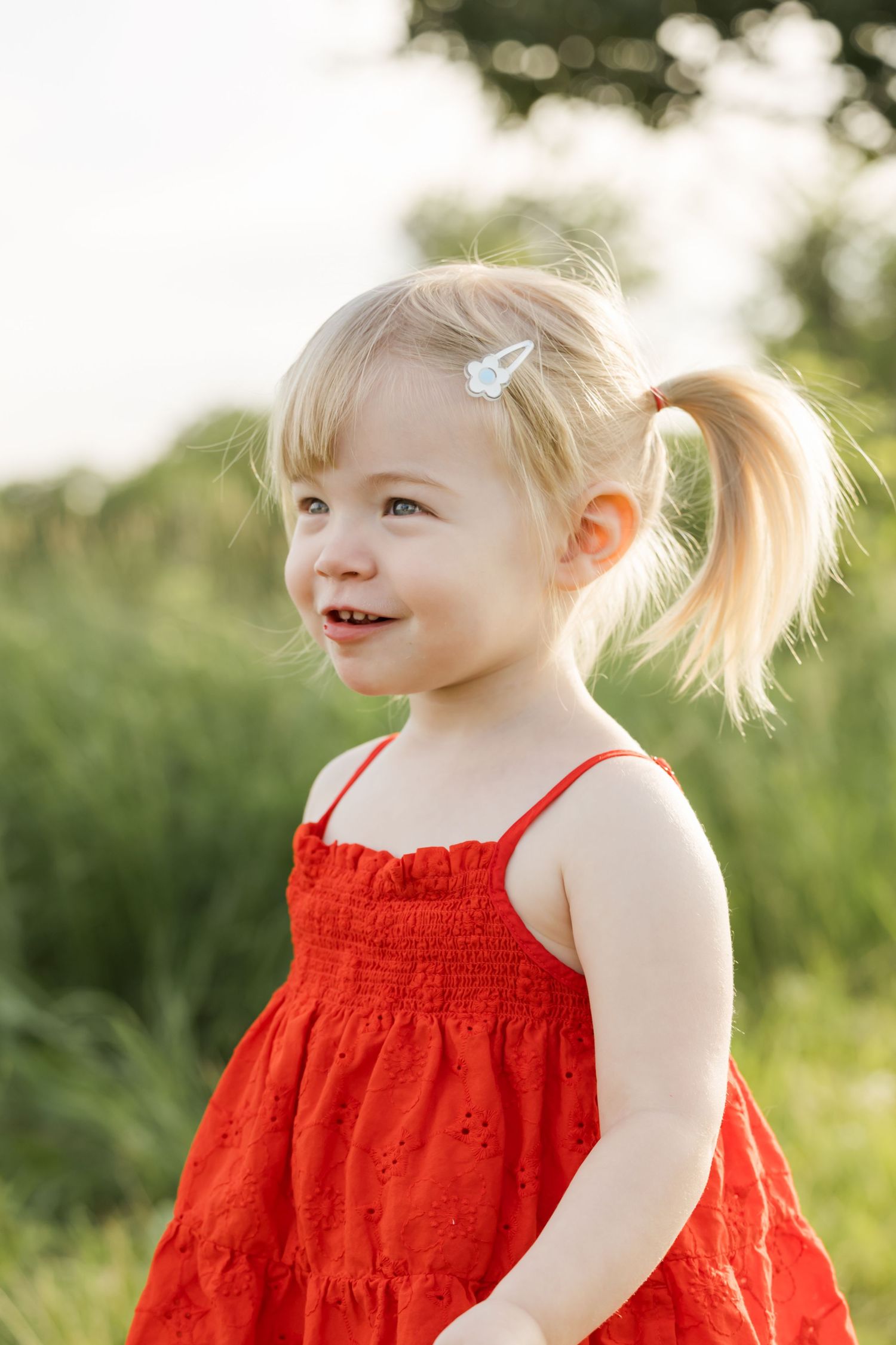 Young child in red summer dress smiling outdoors during golden hour.