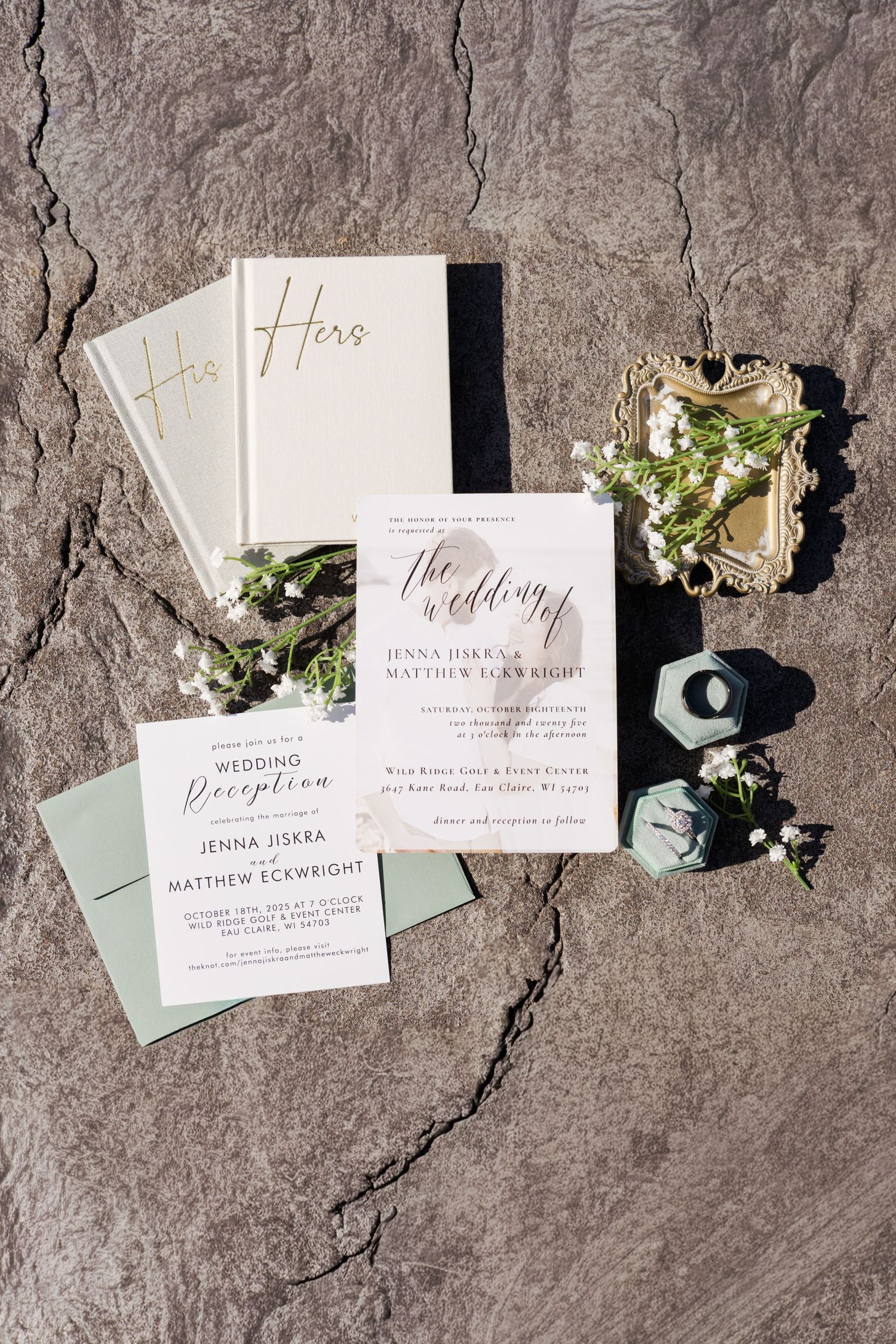 Elegant wedding invitation suite with white and gold lettering laid out on stone surface.