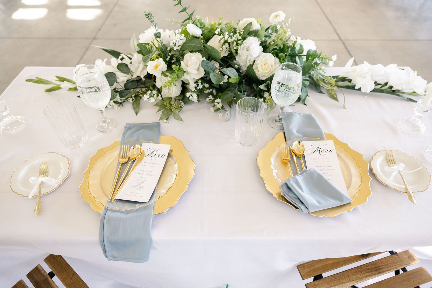 Elegant white wedding cake decorated with fresh flowers and greenery on a rustic wooden stand.