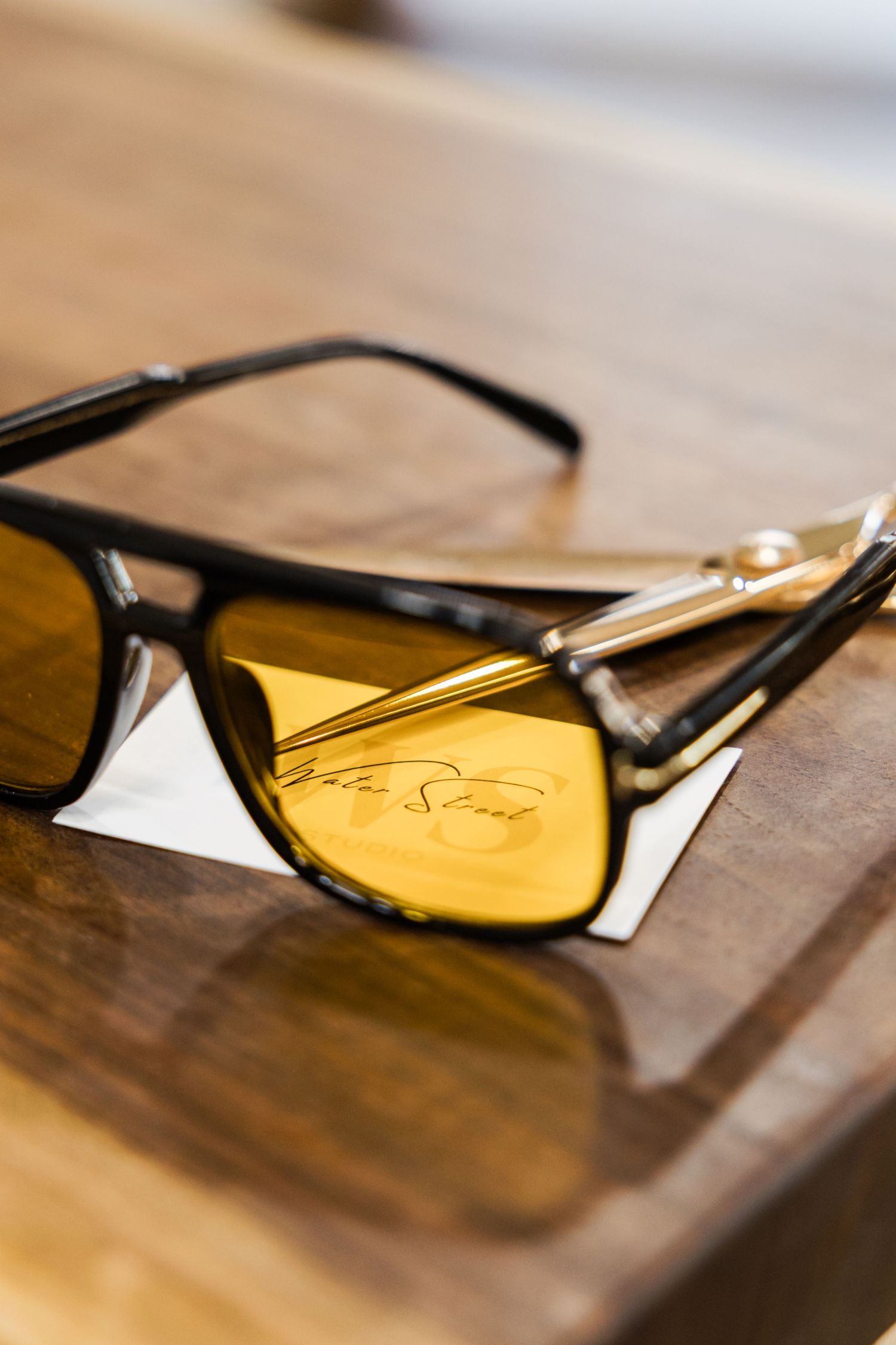 Yellow-tinted sunglasses with black frames rest on a wooden surface in a series of artistic close-up shots.