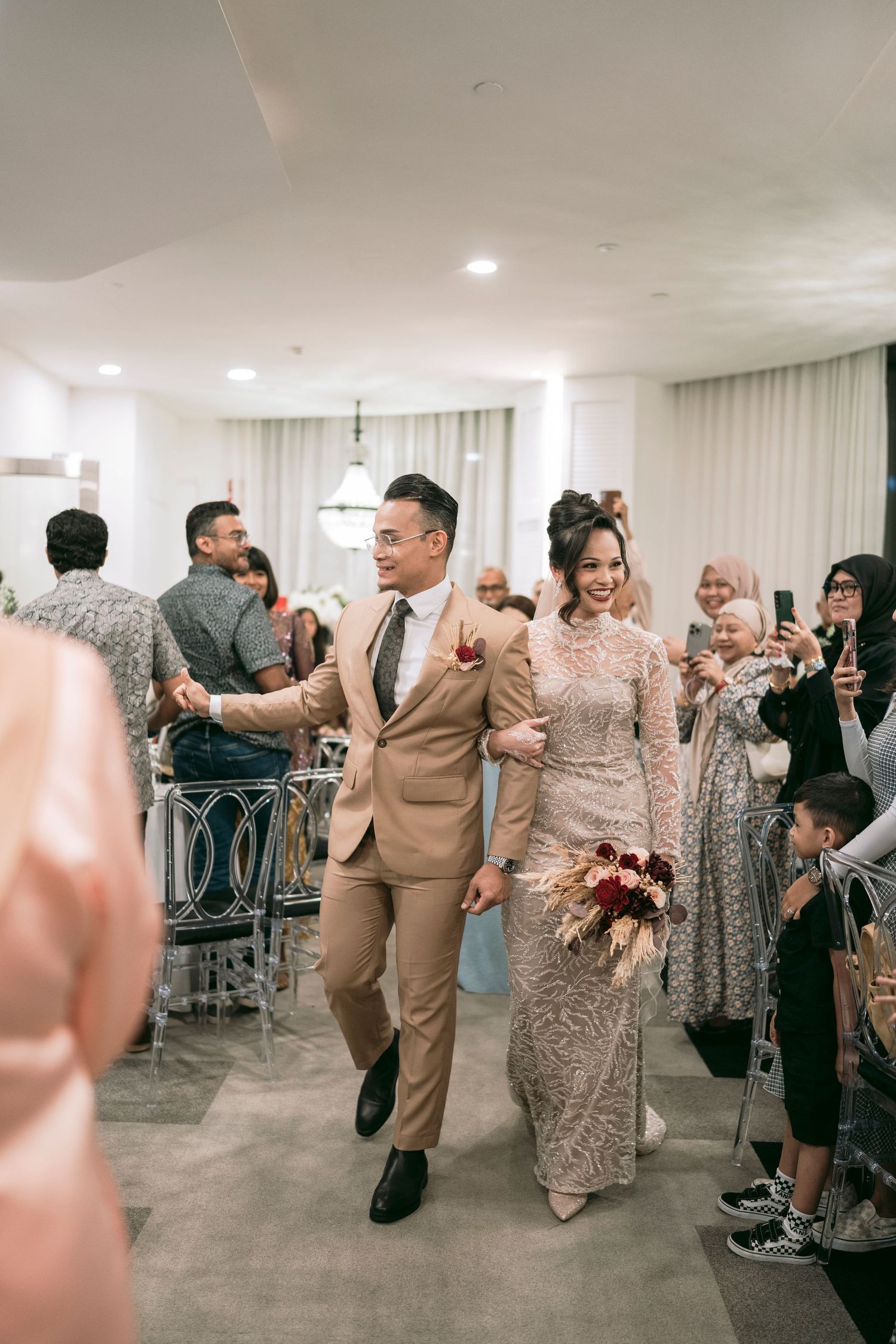 A couple walks down a hallway as they celebrate in elegant beige and sparkling formal attire at Malay wedding Novotel on Stevens.