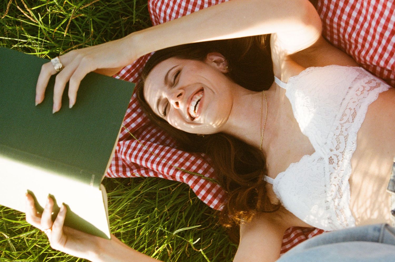 Person lying on red checkered blanket in grass during sunny afternoon.