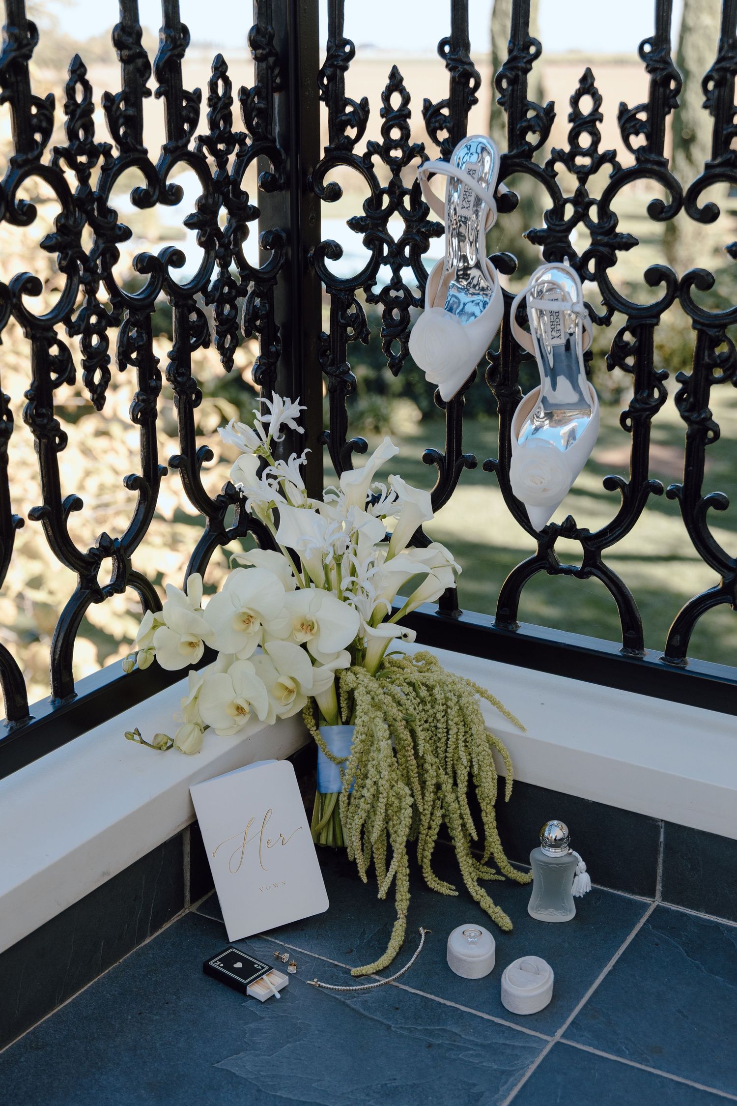 Elegant wedding decor features white orchids, hanging crystal shoes, and ornate black iron gates against a soft background.
