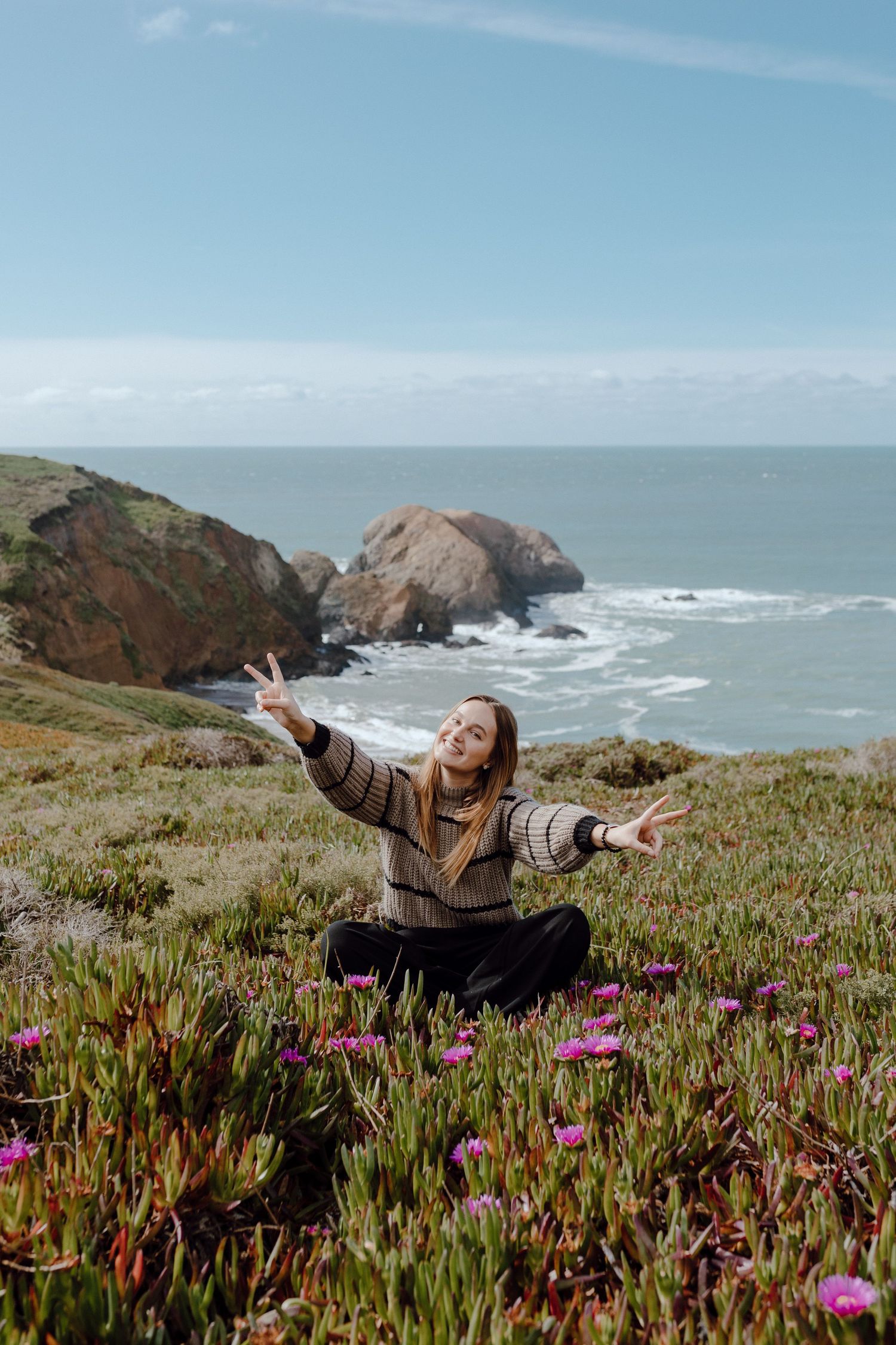 Person enjoying the coastal views while lying in a field of pink wildflowers along the rugged California coastline.