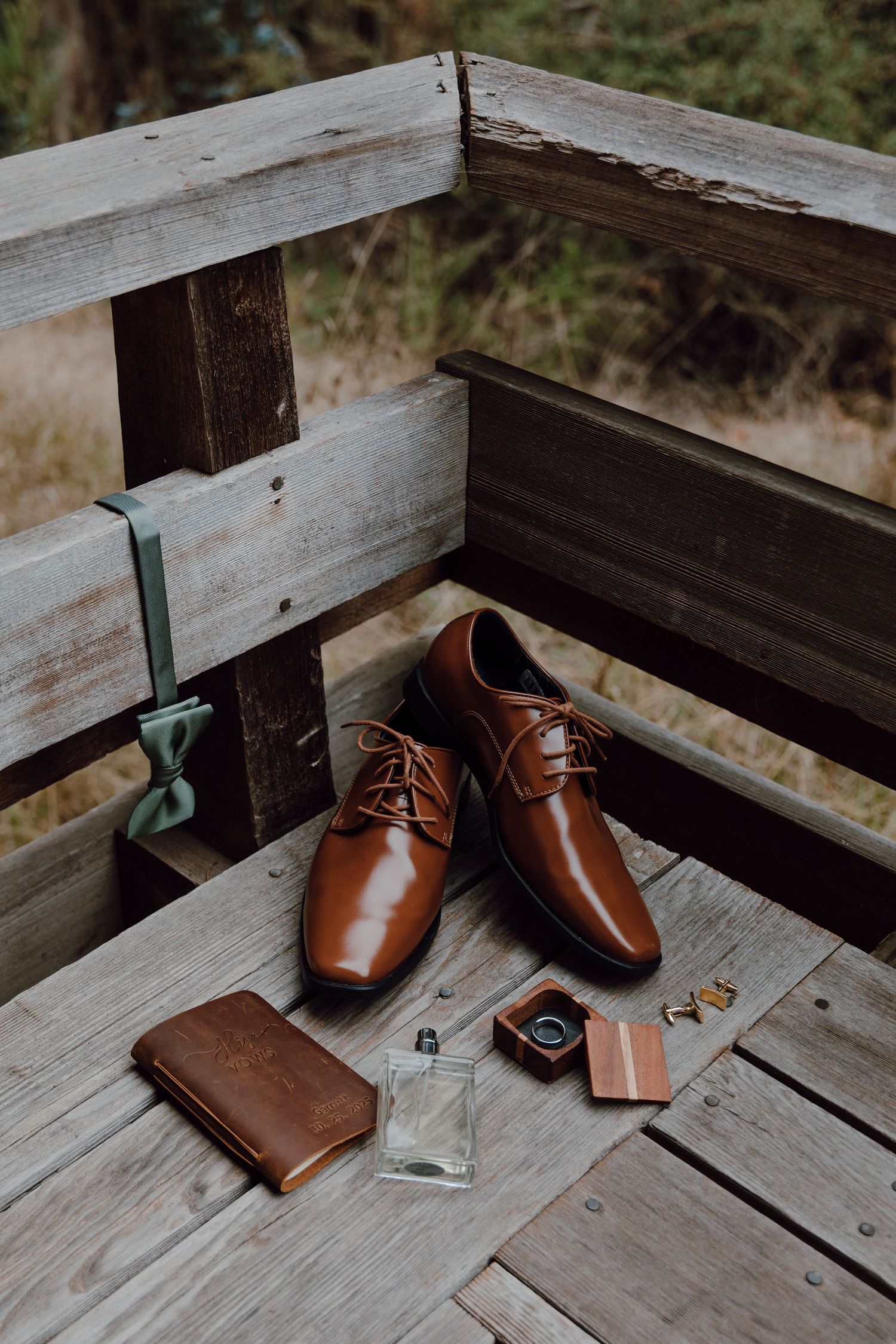 Brown leather dress shoes and wallet arranged on rustic wooden deck in natural lighting.