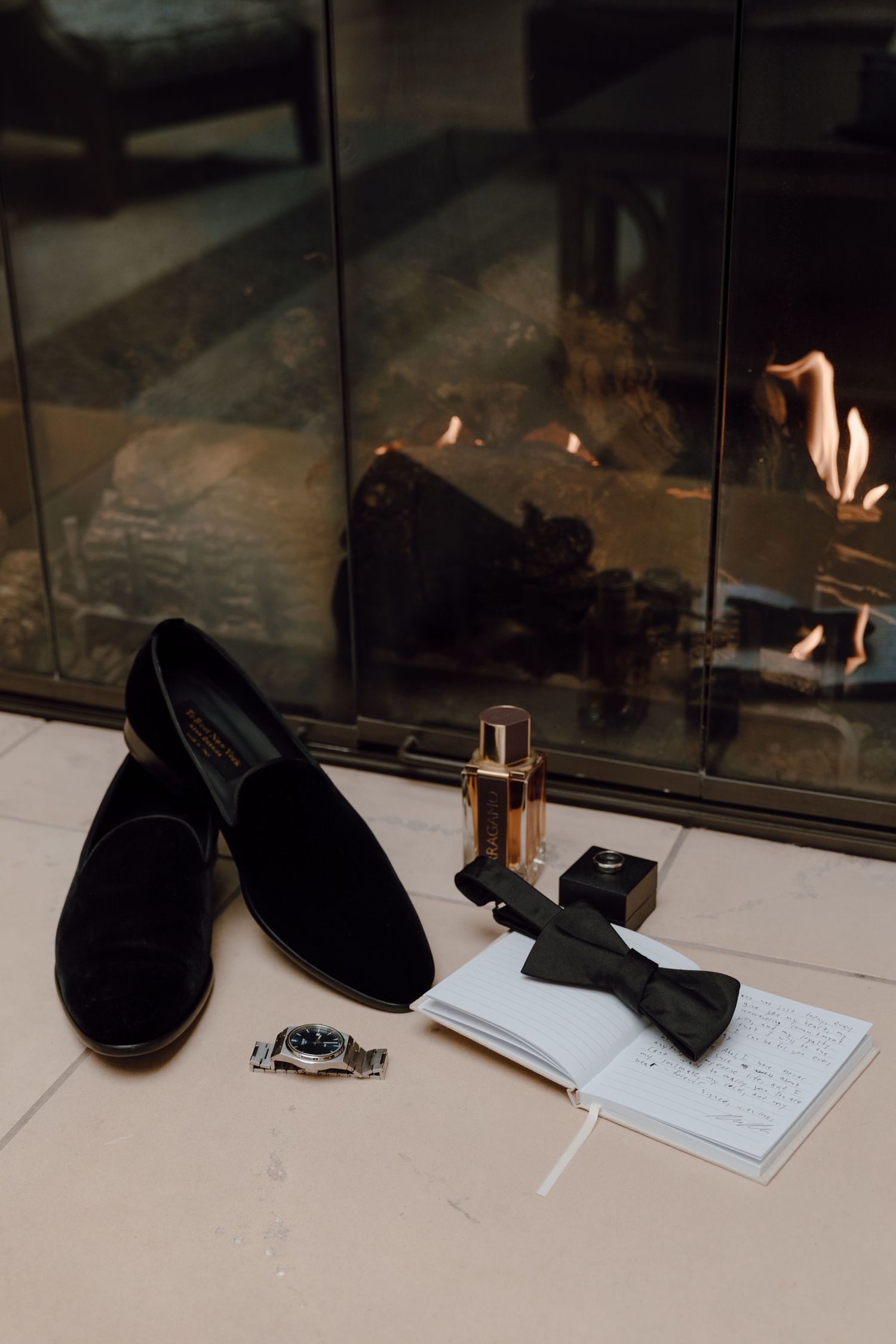 A pair of black suede loafers sits beside papers and small objects on a white surface near a glass partition.