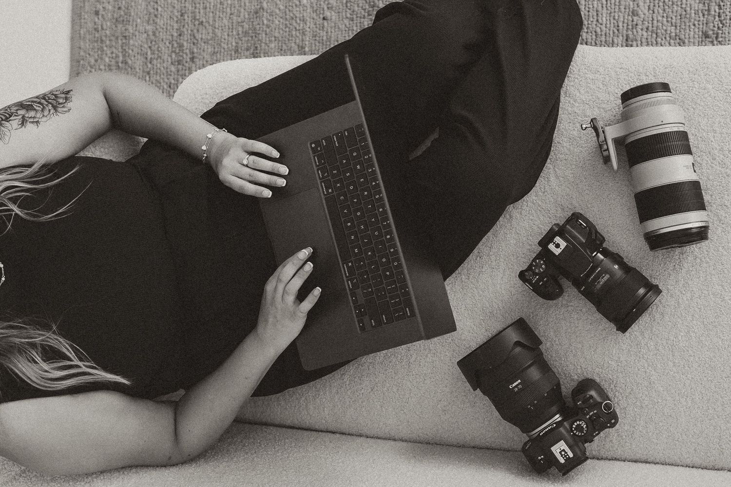 Black and white overhead shot of photographer working on laptop with cameras on couch.