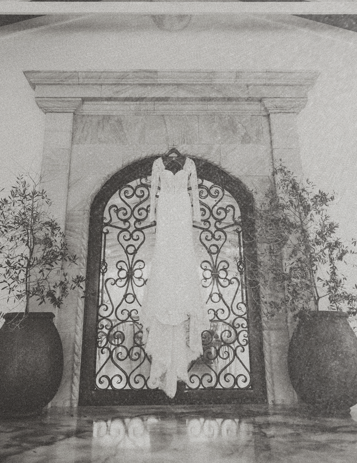 Elegant wedding dress hanging on ornate wrought iron door in a grand arched entryway with marble surround.