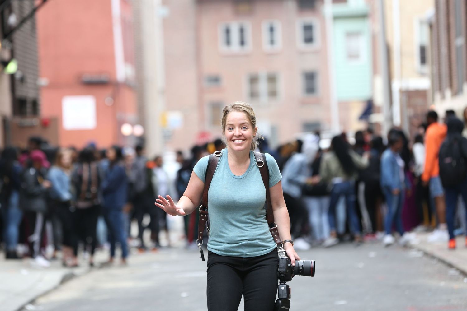 A photographer with camera equipment walks through a crowded urban street.