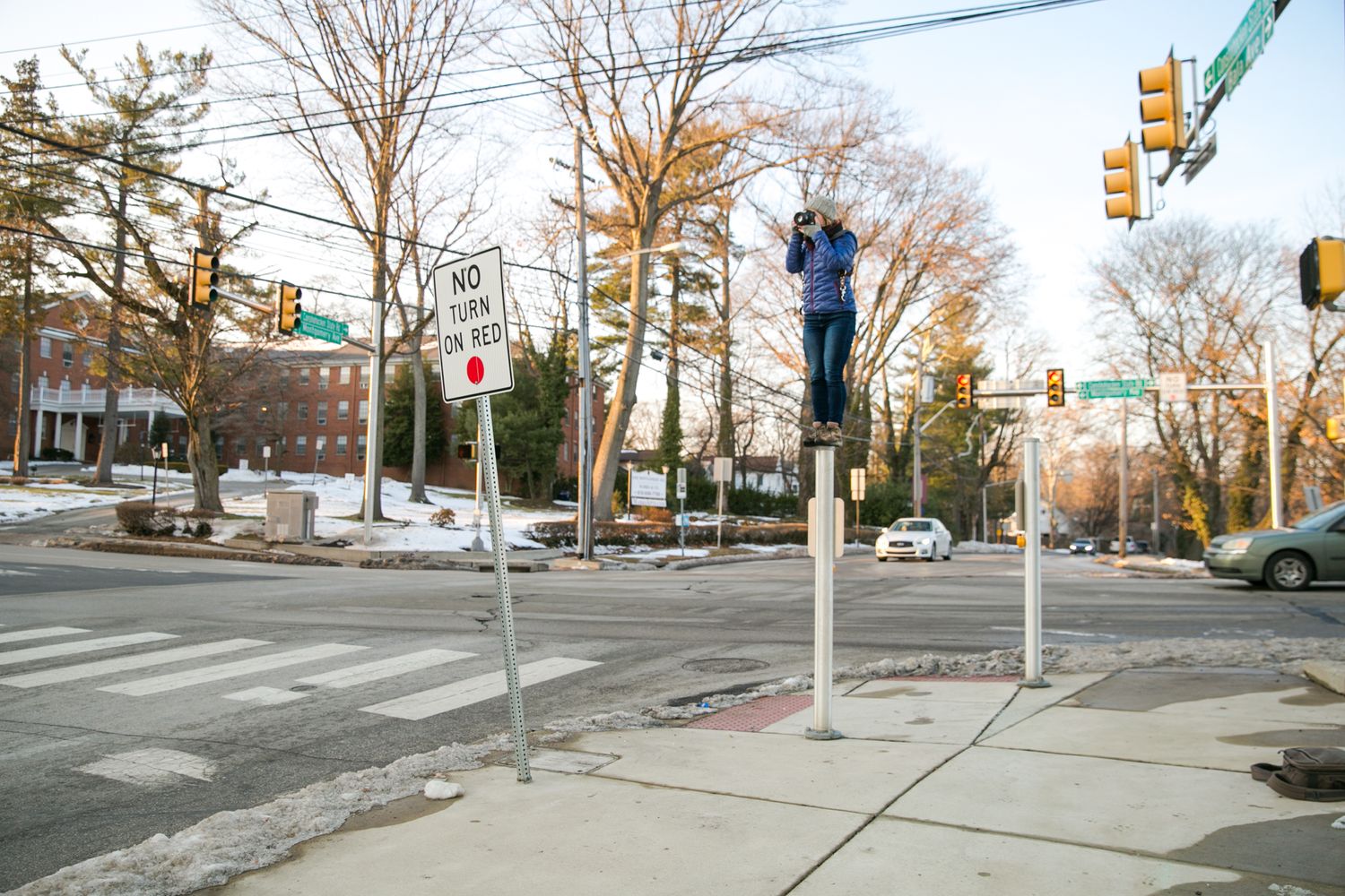 A winter street intersection with traffic lights and bare trees against a cloudy sky.