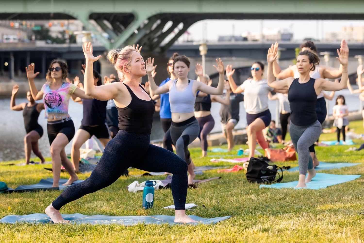 Large group practicing yoga poses together on grass during outdoor fitness class.