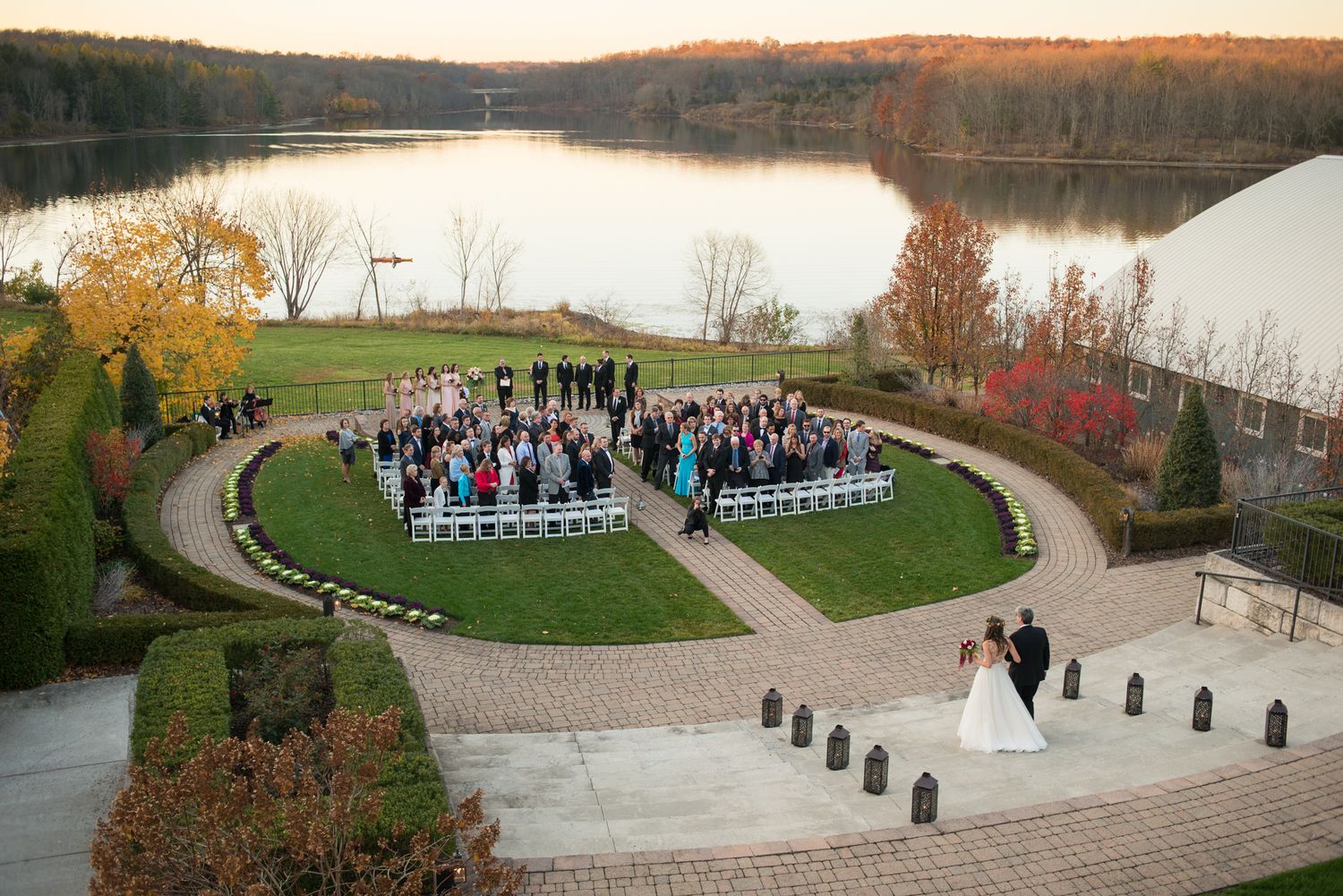 Panoramic view of an outdoor wedding venue with rows of white chairs at sunset.