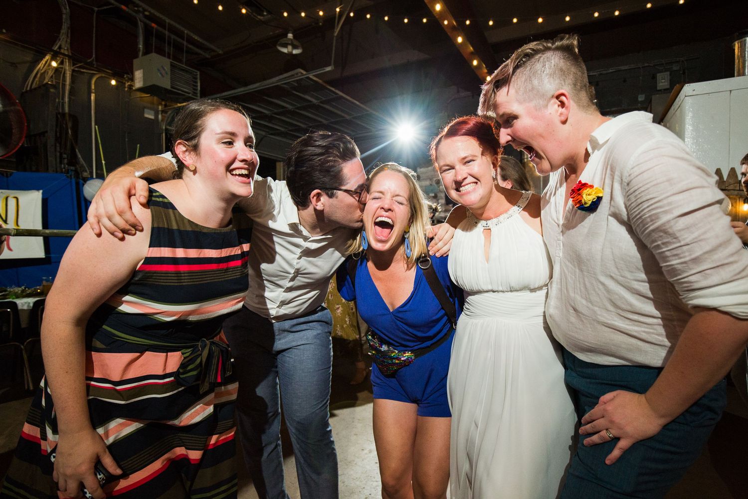 Wedding guests dancing enthusiastically under warm string lights at an evening reception.