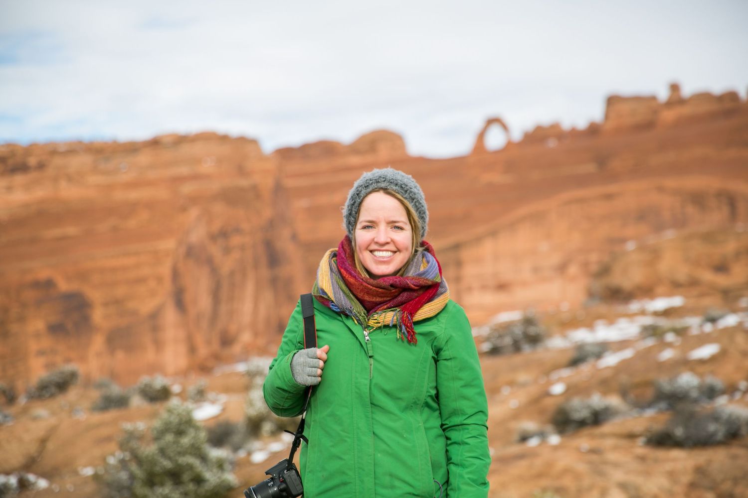 Person in bright green jacket exploring snowy red rock formations in winter.