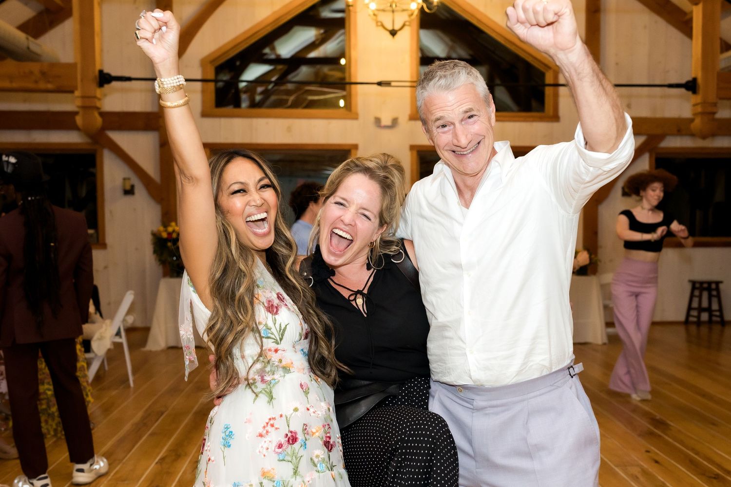 Three people celebrate with raised arms in a rustic wooden interior.