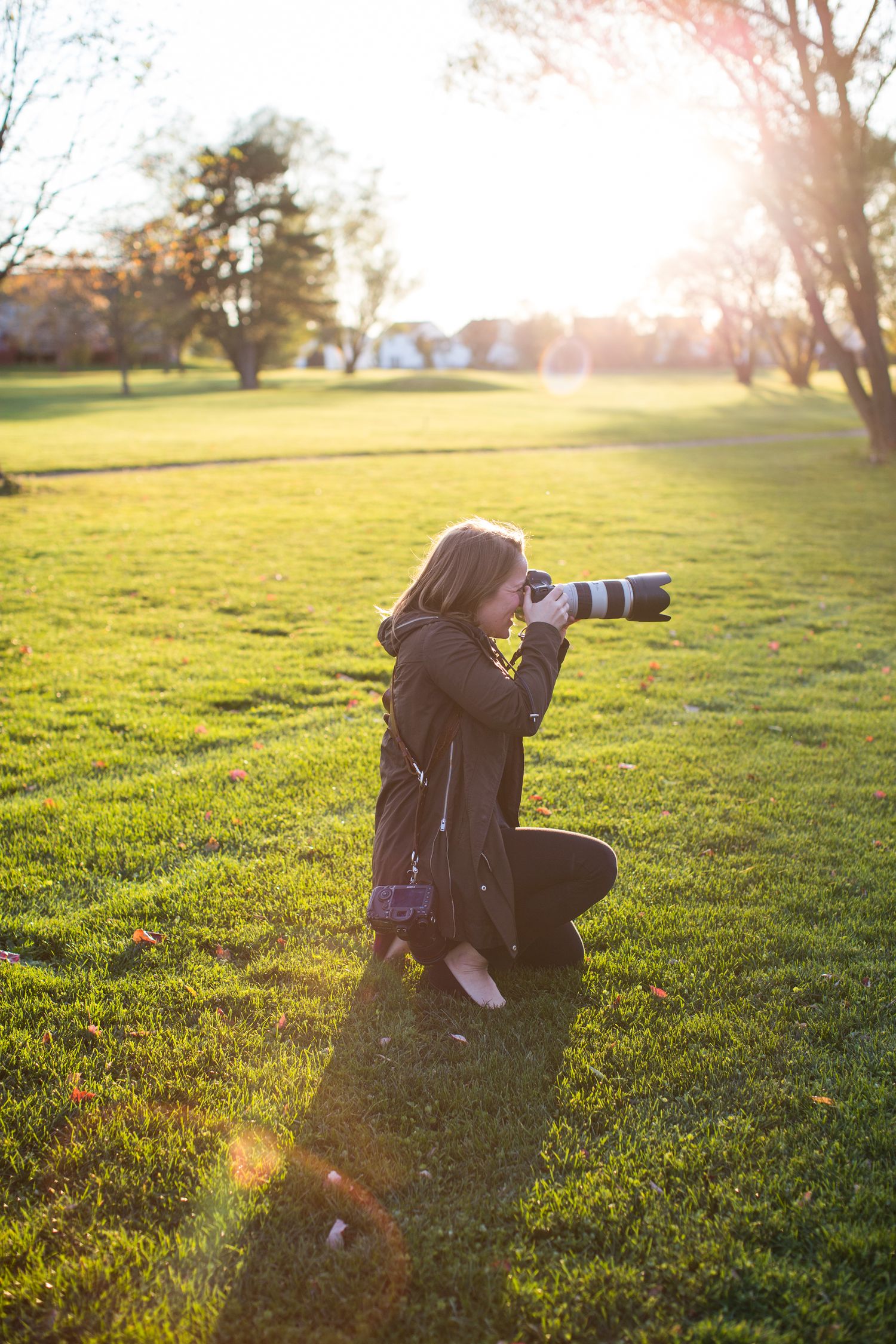 Photographer silhouetted against golden sunset light while taking pictures in a grassy field.