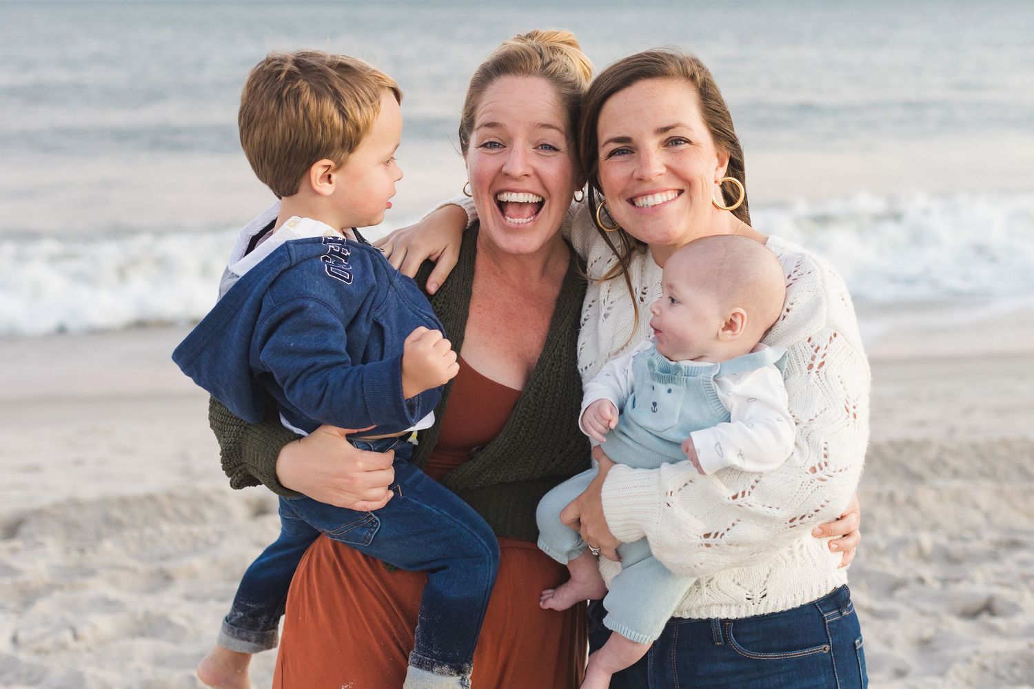 Happy group poses together on beach with ocean waves in background.
