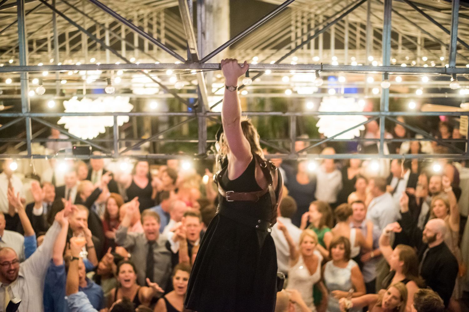 Performer in black dress raises arms triumphantly before an energetic crowd.