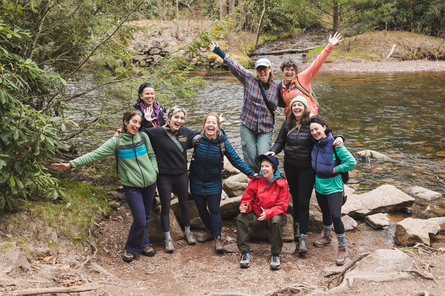 Group of friends posing with outstretched arms by a rocky stream in nature.