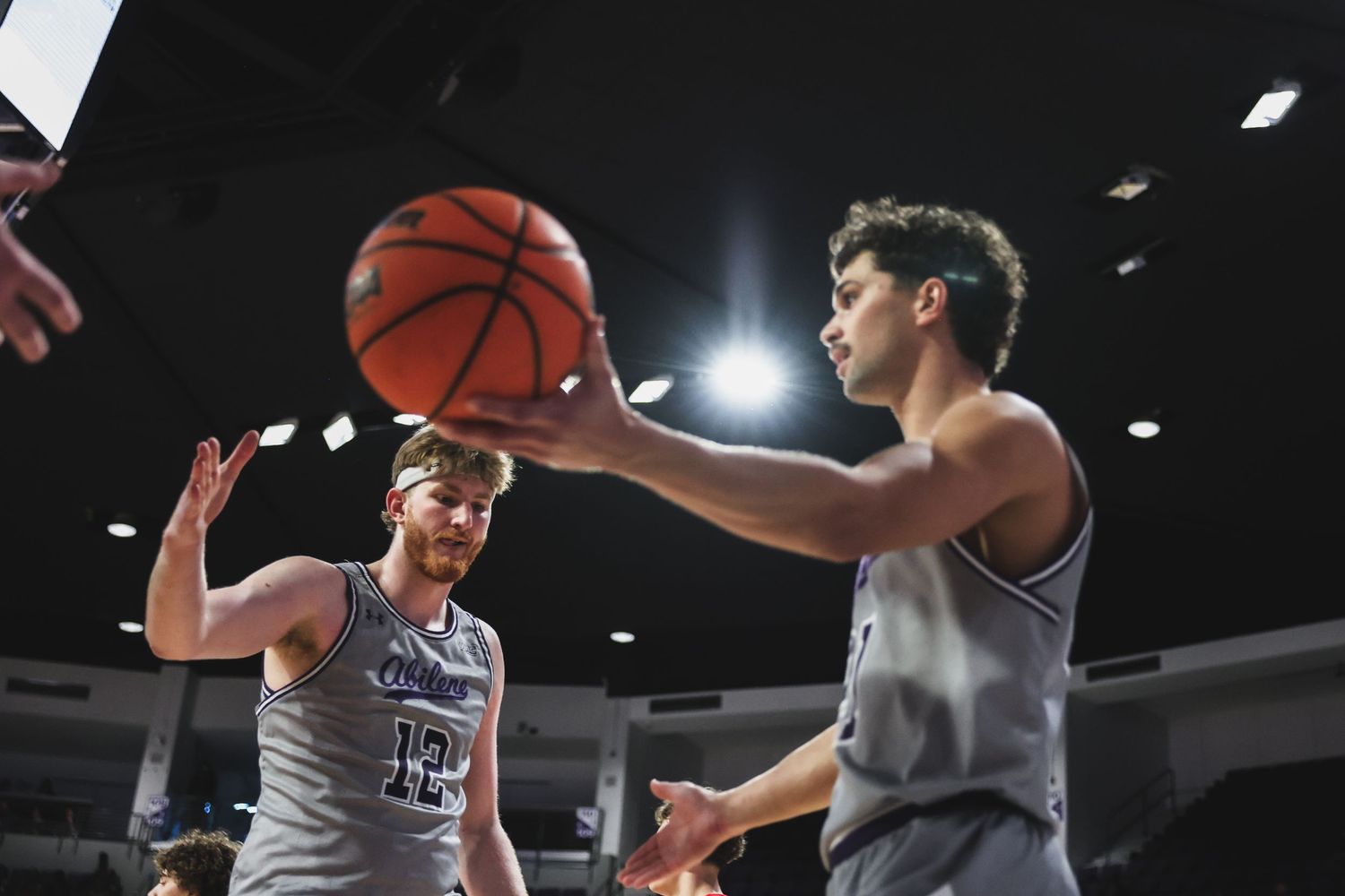 Two Abilene Christian basketball players practice passing drills during warmups in an indoor arena.