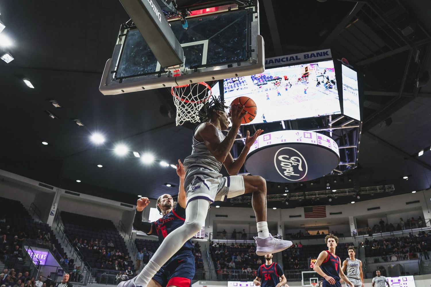 Basketball player in gray uniform attempts a powerful dunk during a college basketball game in a packed arena.