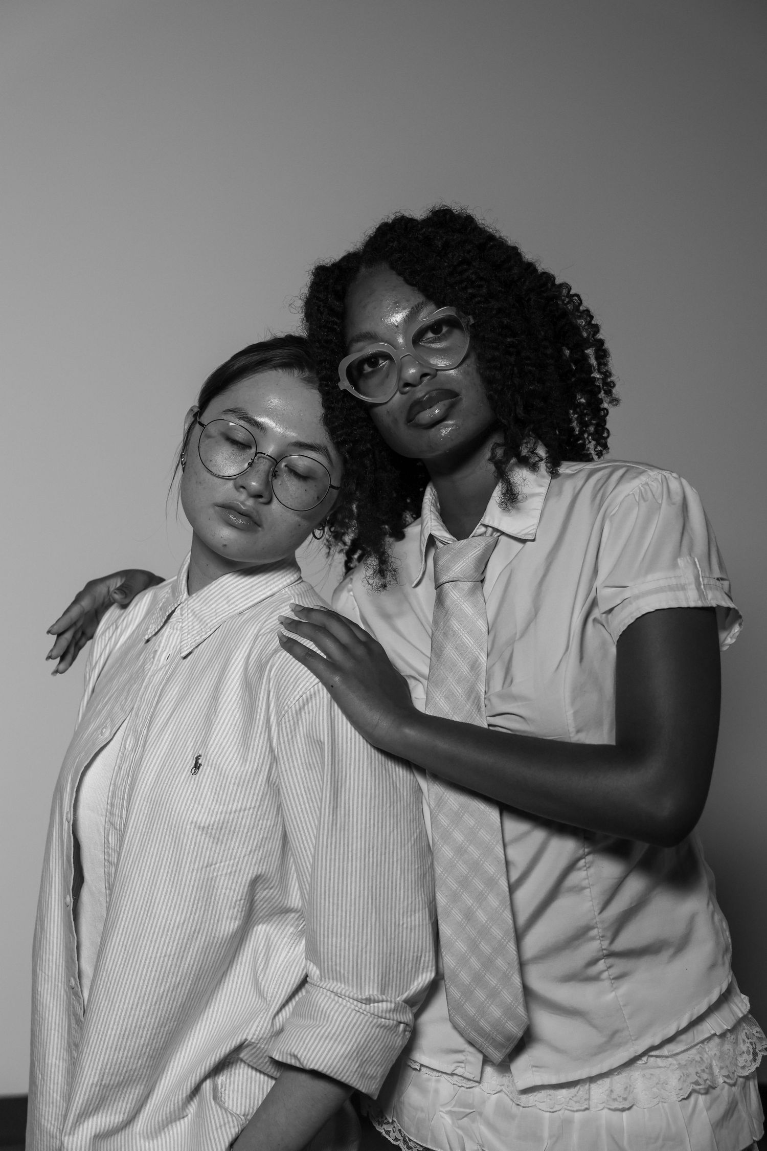 Black and white portrait of two women wearing glasses and button-up shirts posing together.