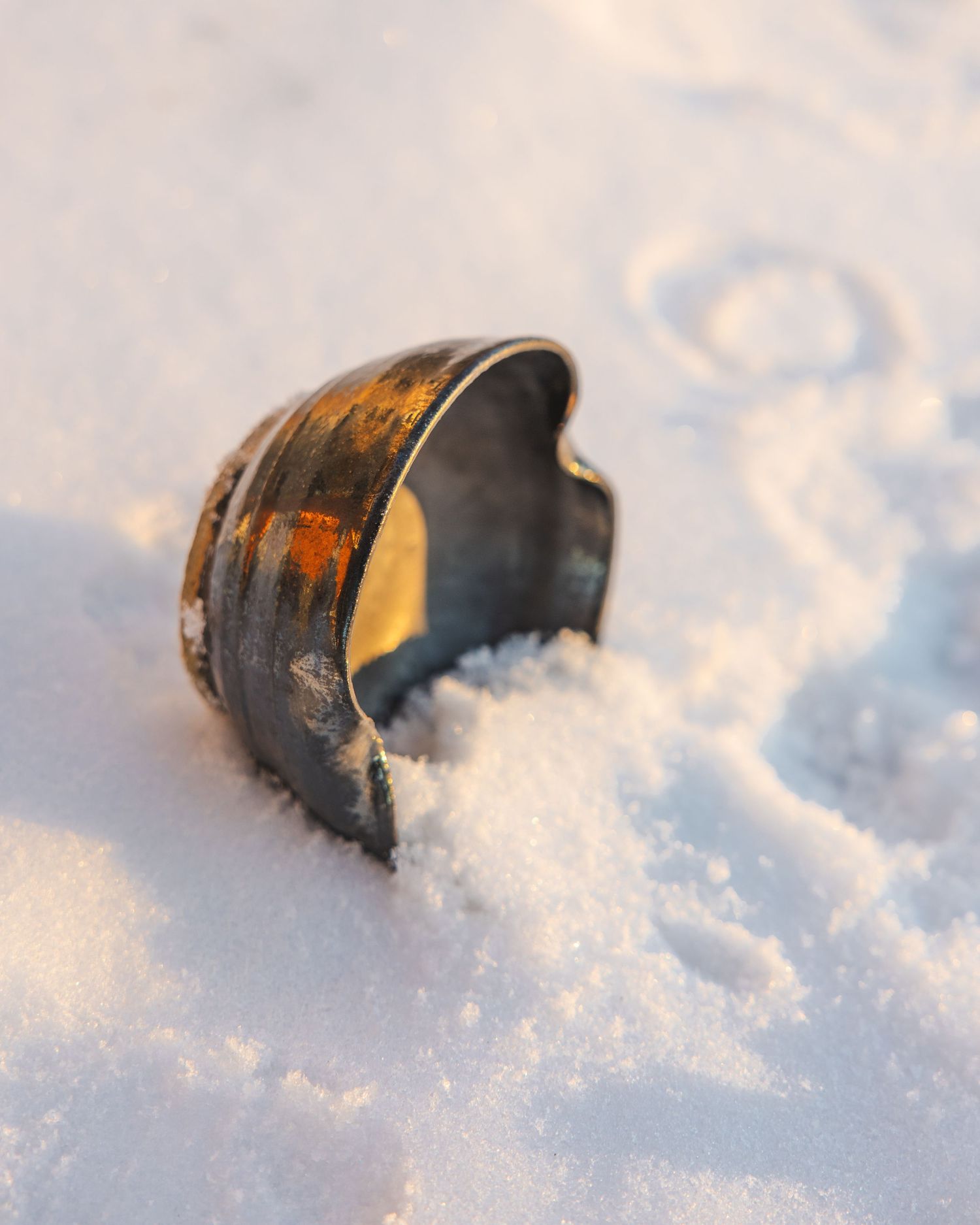Dark metallic ceramic cuff bracelet with copper accents partially buried in snow.