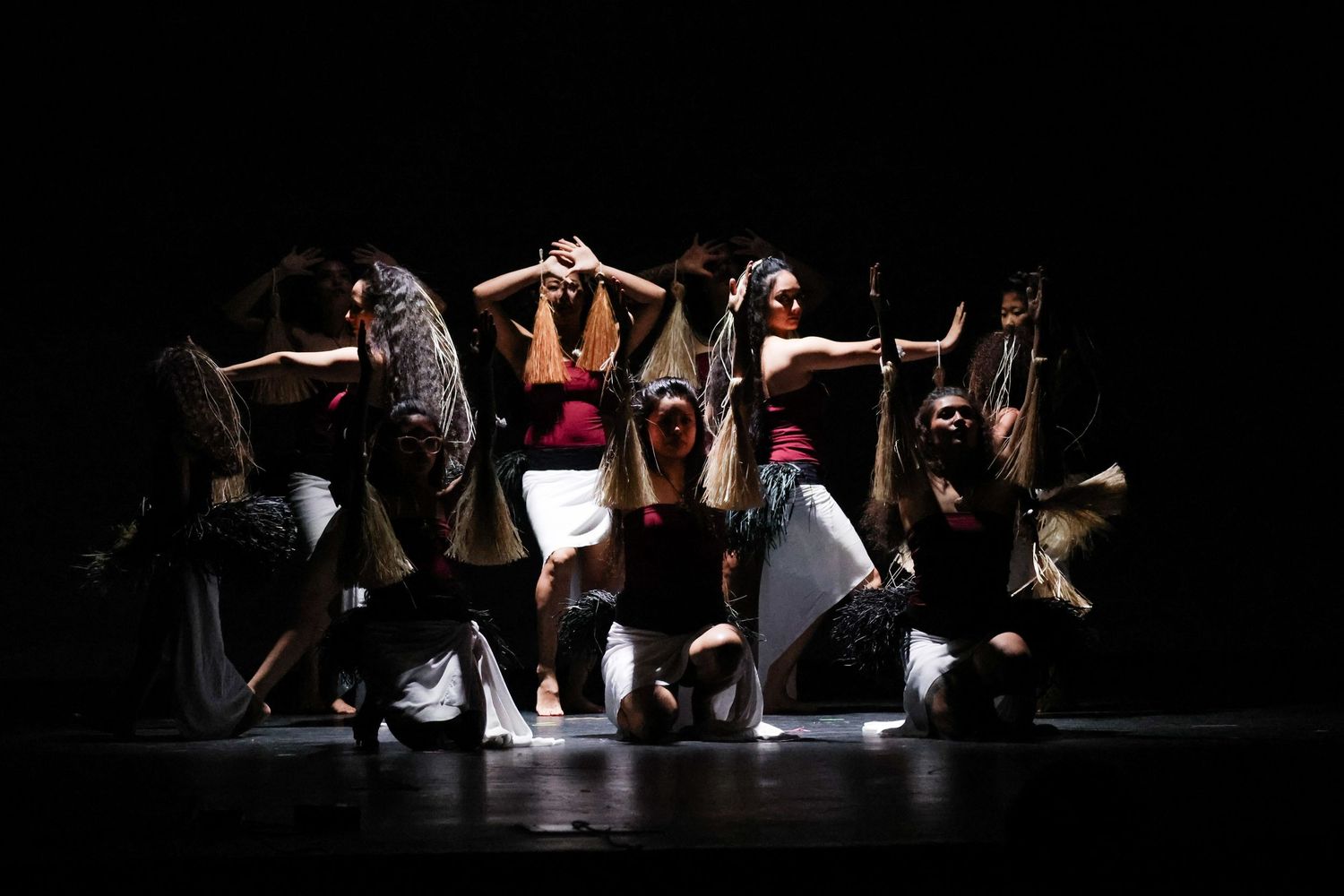Group of dancers in a striking formation on a dimly lit stage in expressive costumes.