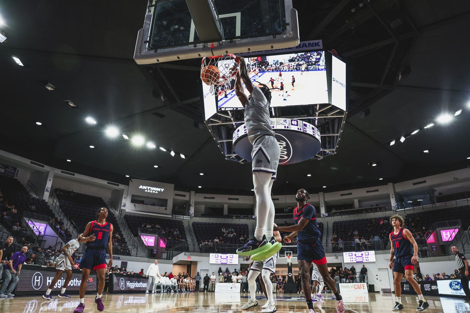College basketball player completing a thunderous dunk over defenders during an intense arena game.