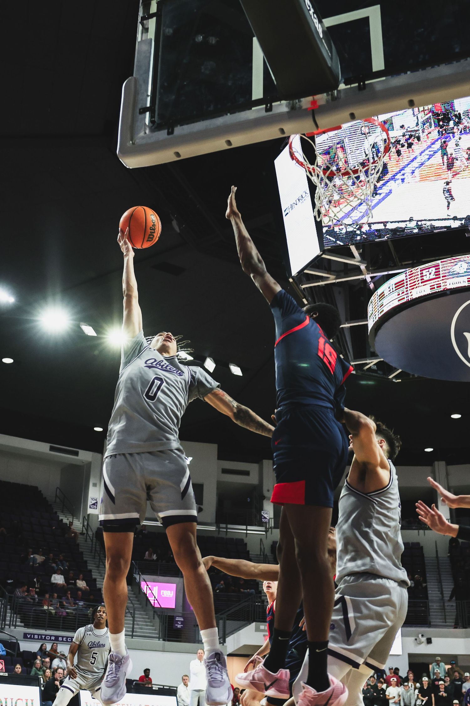 Abilene Christian player number 0 attempts a shot while being challenged by a Texas Tech defender.