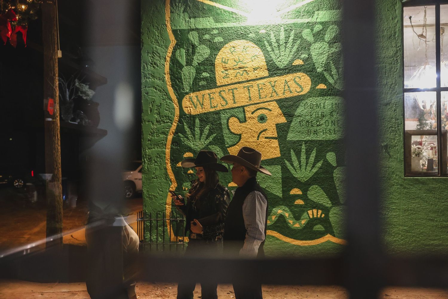 Two people standing in front of a vibrant green West Texas mural at night.