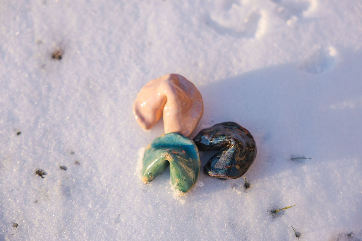 Small handmade ceramic fortune cookie and mushroom sculptures in white snow.