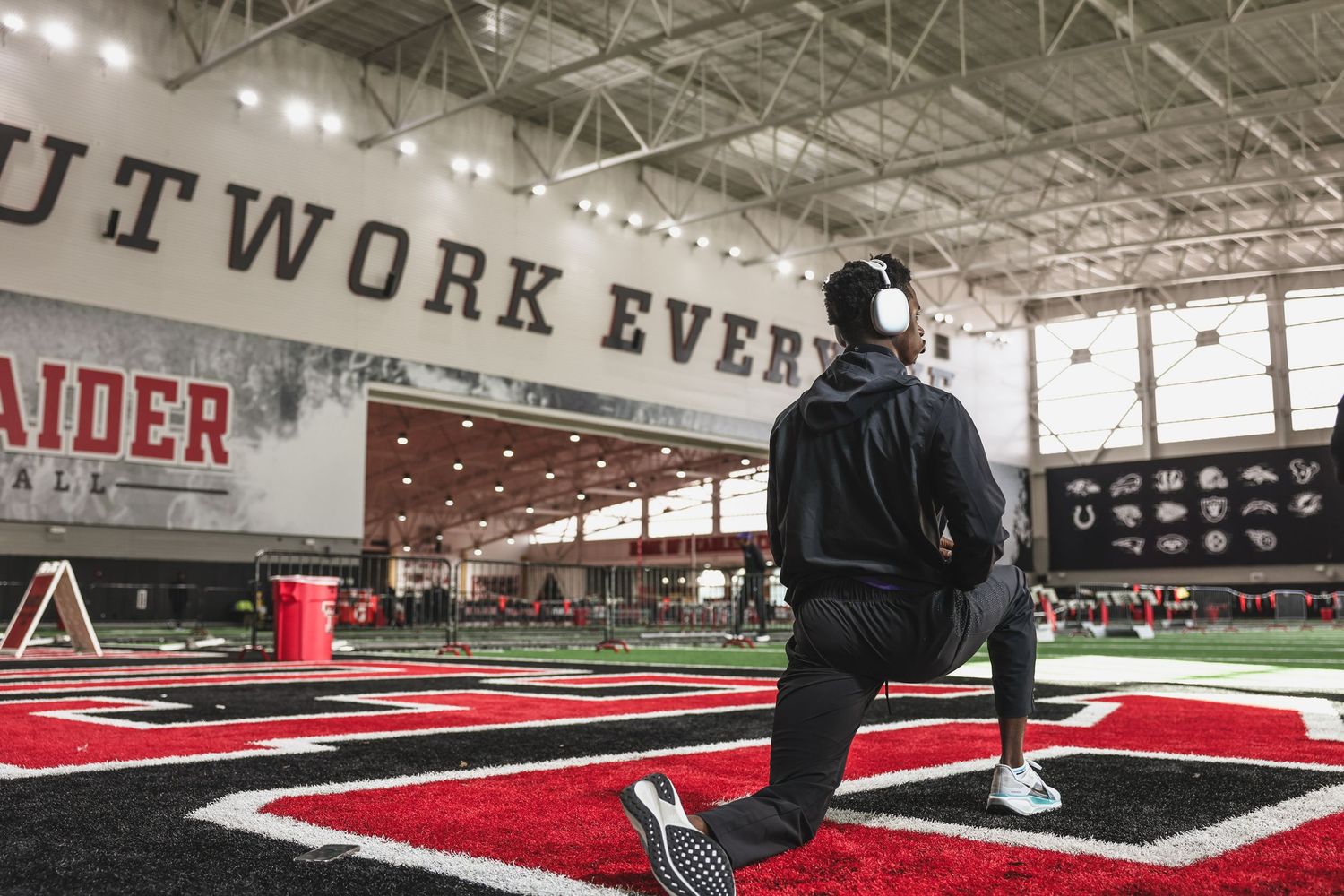 Athlete doing lunges in Texas Tech Red Raiders indoor facility wearing headphones and black jacket.