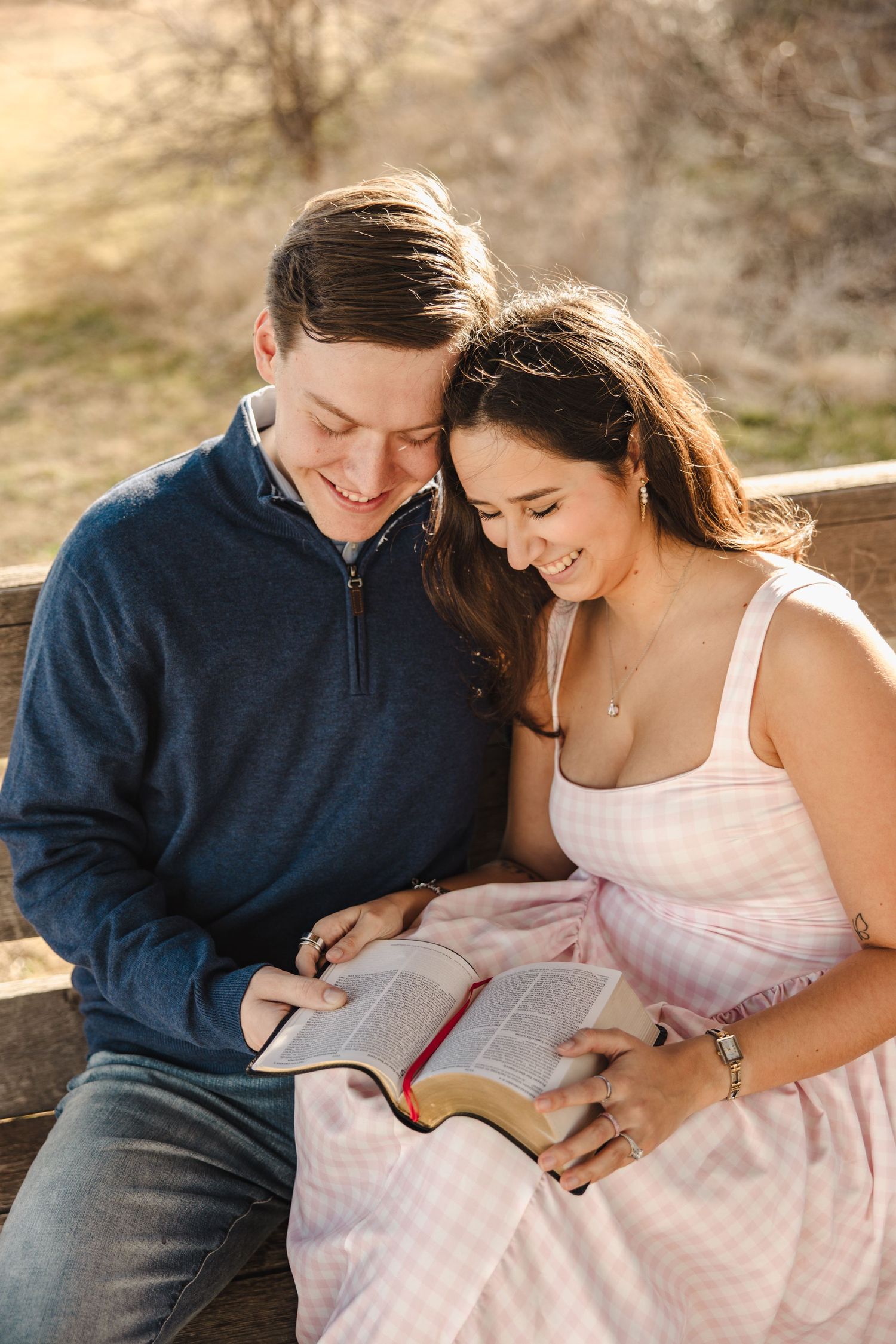 Smiling couple reading a Bible together on a bench in warm outdoor sunlight.
