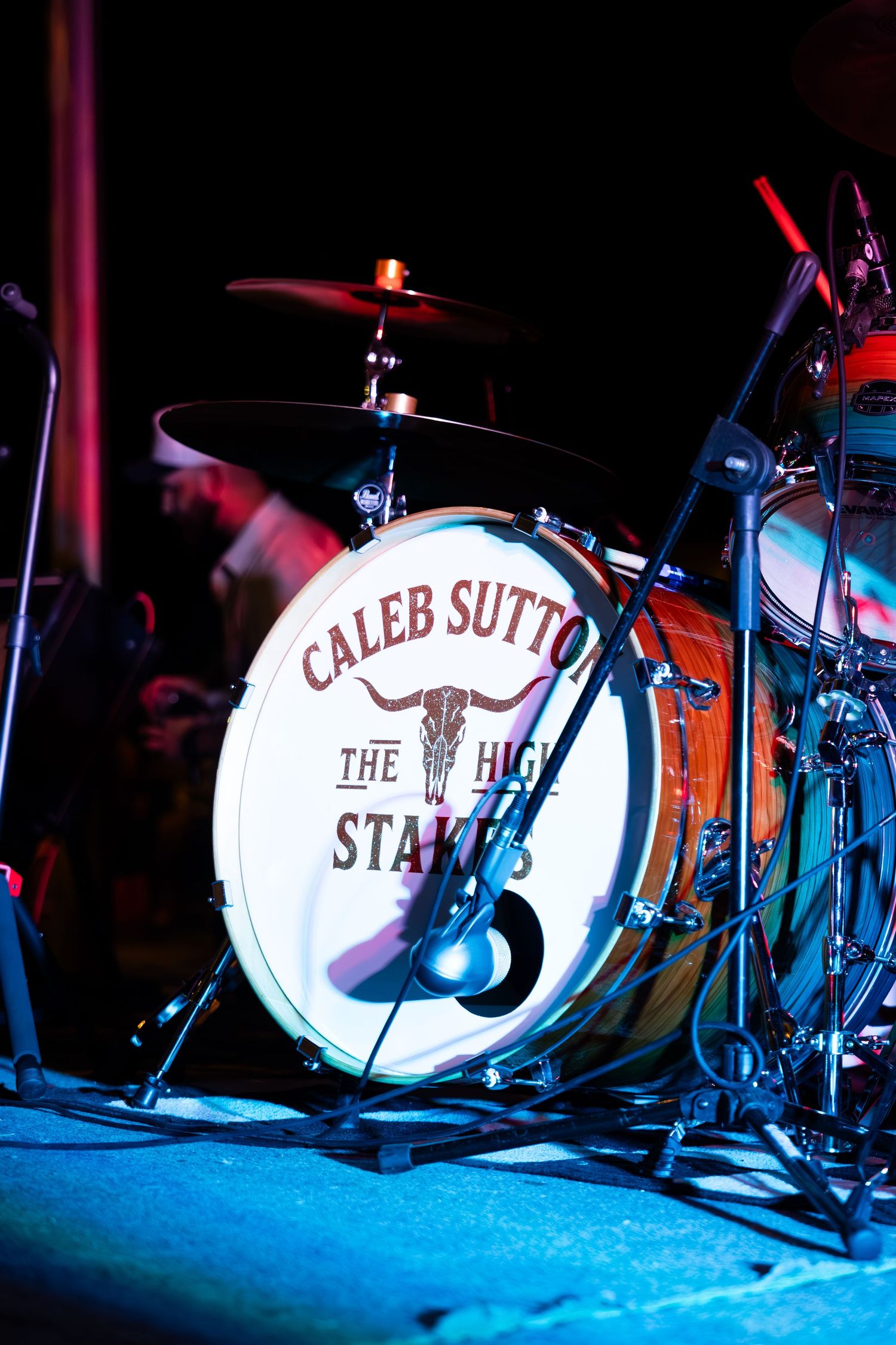 Caleb Sutton and The High Stakes branded bass drum head on stage under colorful concert lighting.