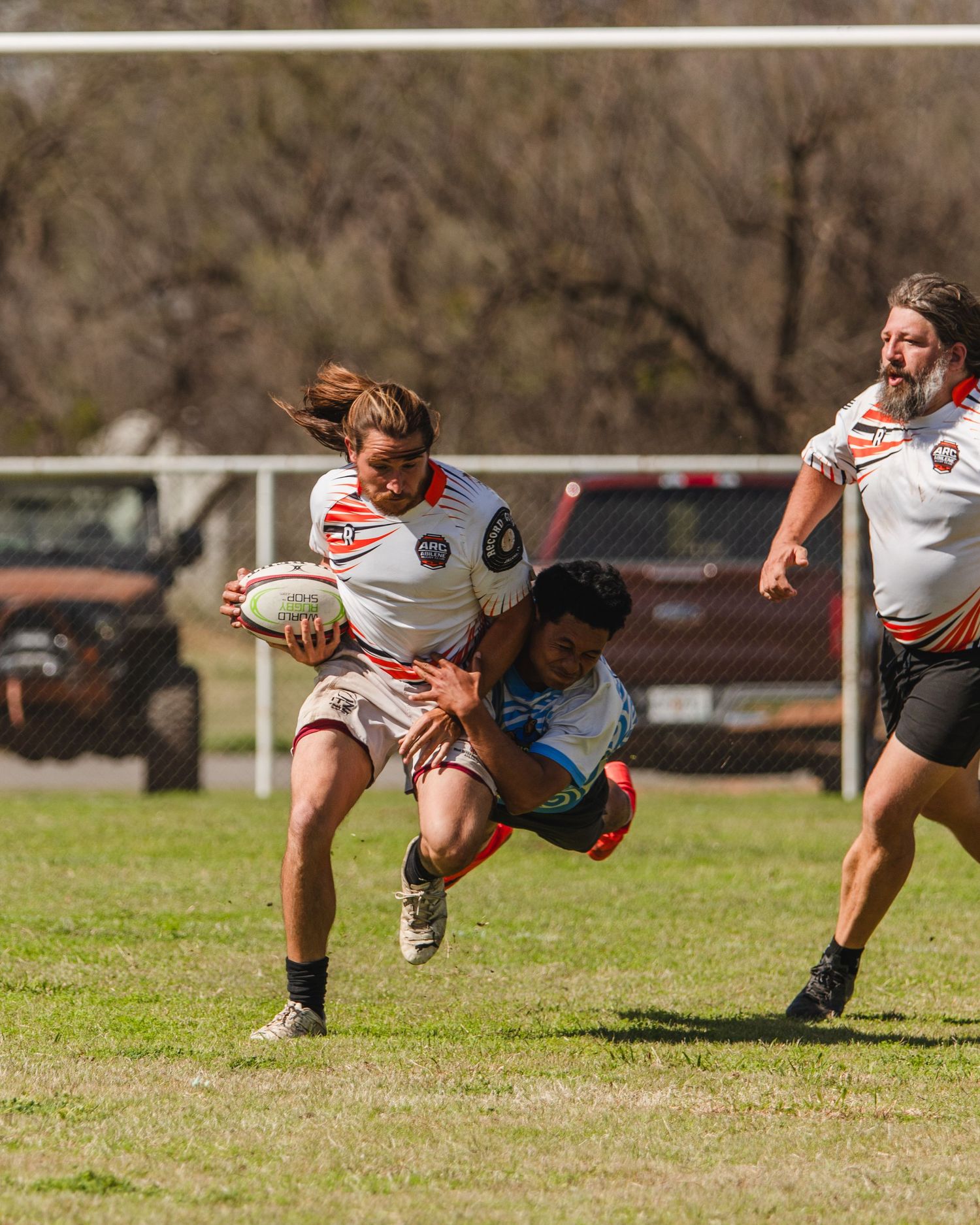 Rugby player carrying ball being tackled during an outdoor match on a grass field.