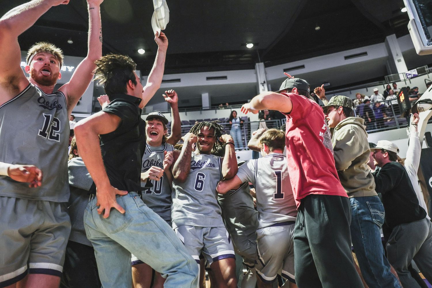 College basketball team and fans rush the court in jubilant celebration after a big victory.