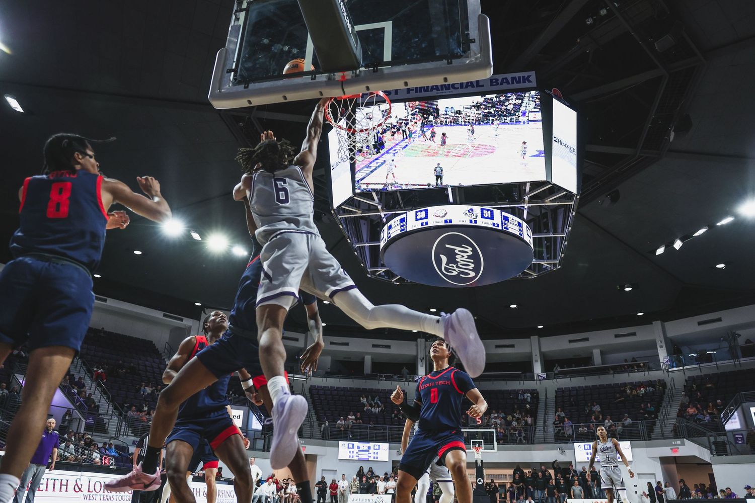 College basketball player number 5 goes up strong for a dunk over defenders in an arena game.