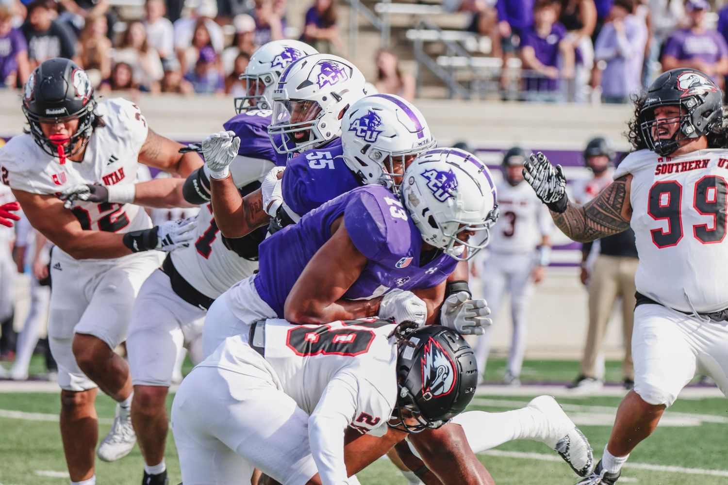 College football players in purple uniforms competing against opponents in white and red jerseys during a game.