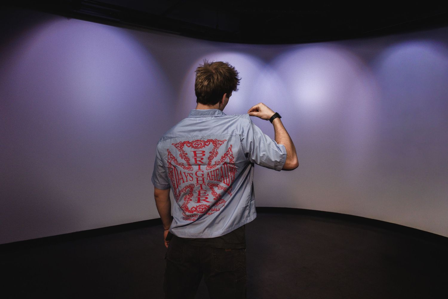 Man viewed from behind wearing gray shirt with red graphic print in curved white room.