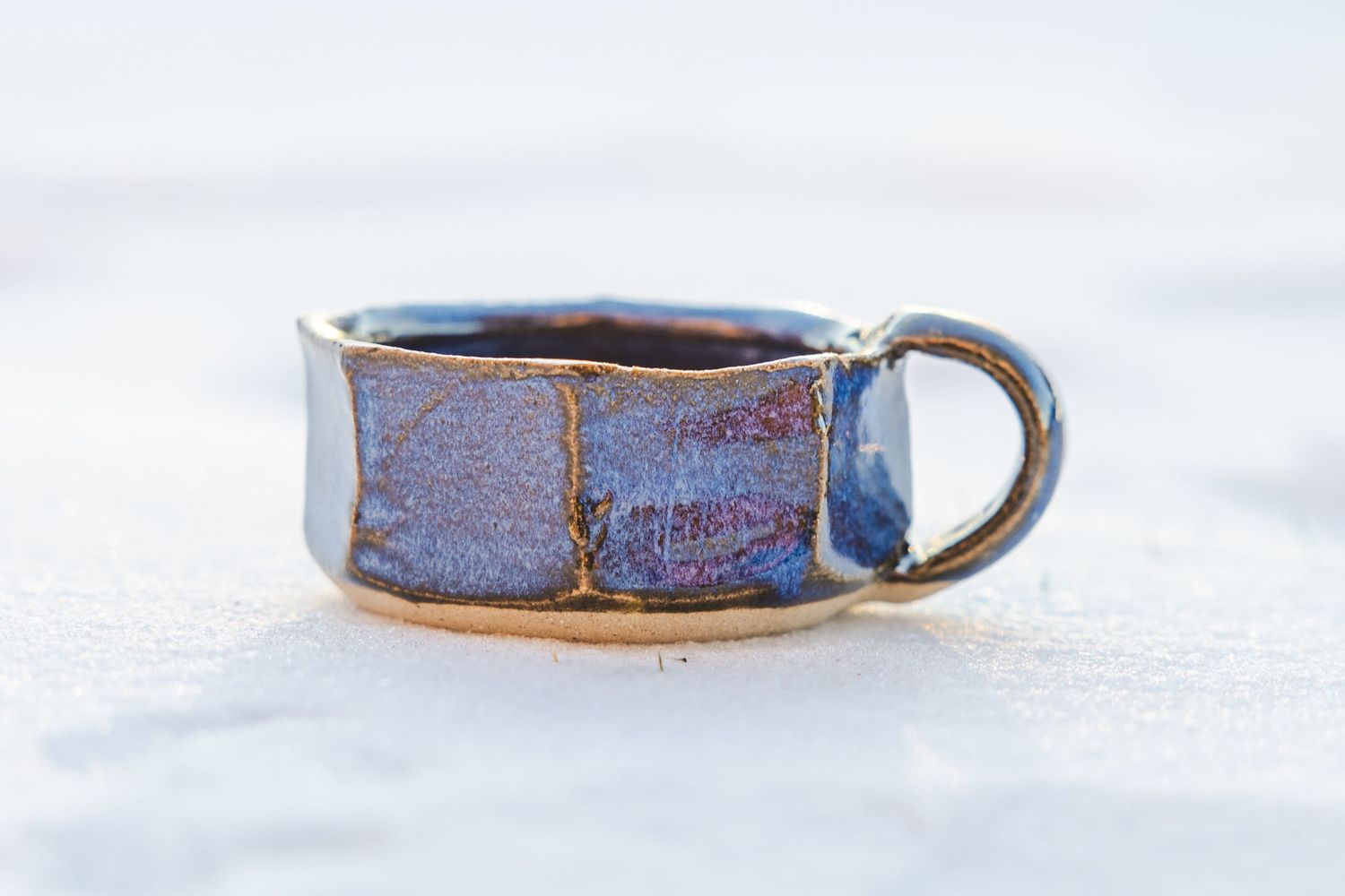 Blue and purple glazed handmade ceramic cup with handle on white surface.