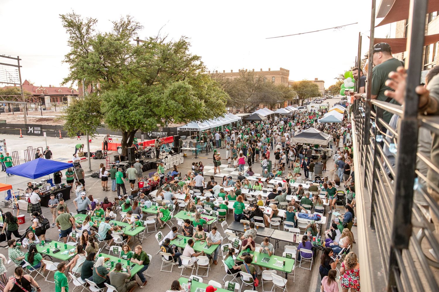 Aerial view of a large outdoor St. Patrick's Day festival with crowds at tables wearing green.