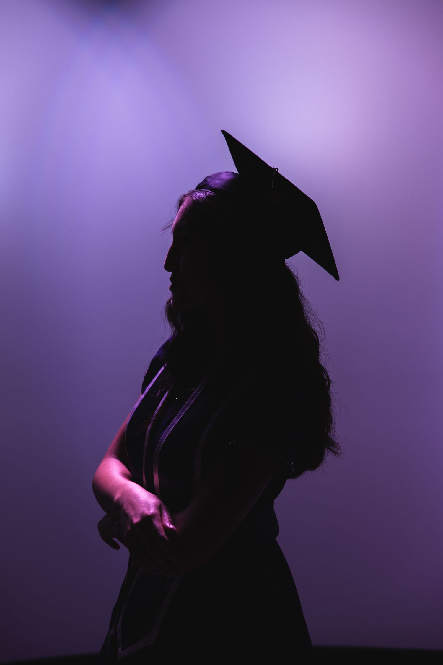 Silhouette of a graduate in cap and gown against a purple-lit background.