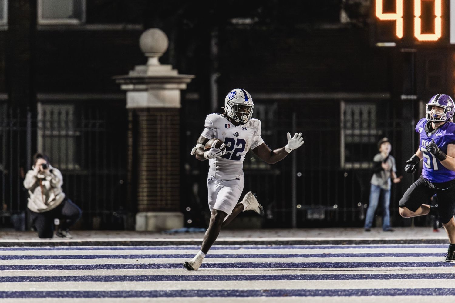 Football player #22 in white uniform breaks away for a touchdown run during a night game.