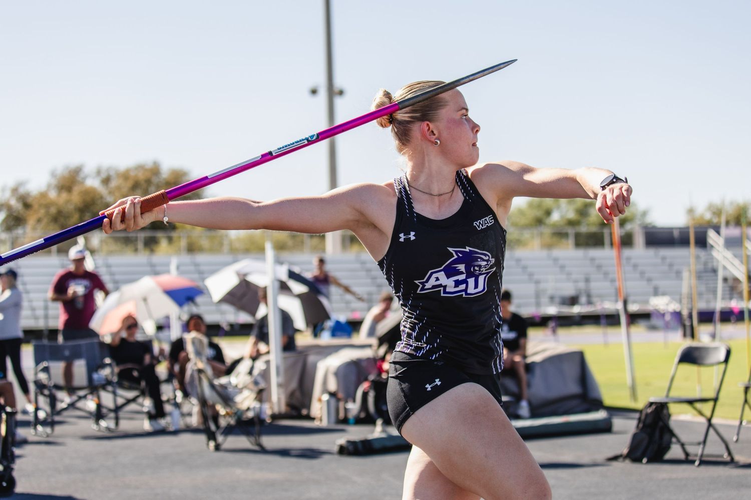 Female athlete in ACU uniform throws a javelin during an outdoor track and field competition.